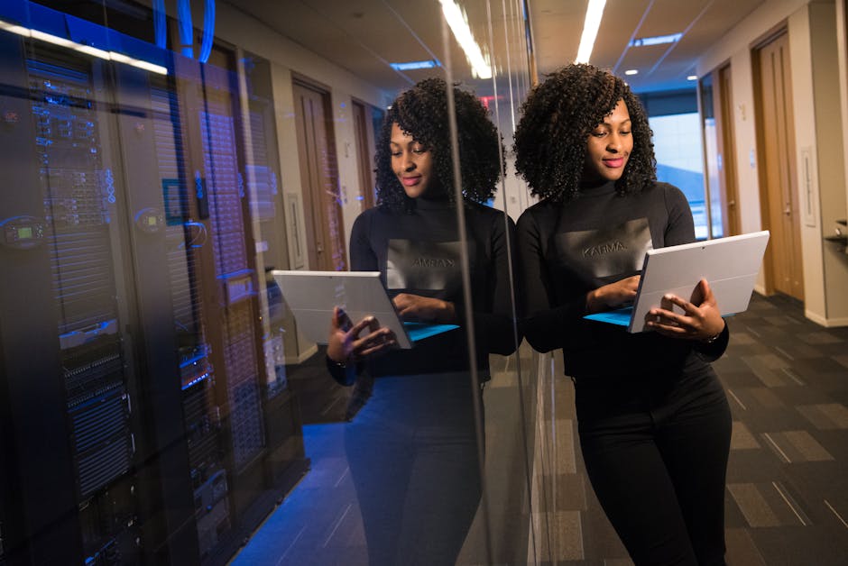 African American woman standing in modern office using laptop, reflecting professionalism and technology engagement.